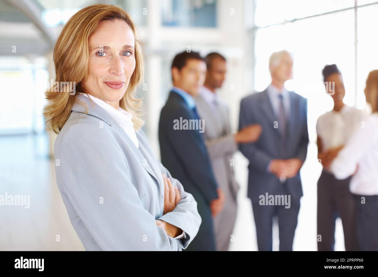Selbstbewusste weibliche Führungskraft mit Geschäftsleuten, die sich unterhalten. Porträt einer selbstbewussten, reifen Geschäftsfrau mit einem Team, das im Hintergrund spricht. Stockfoto