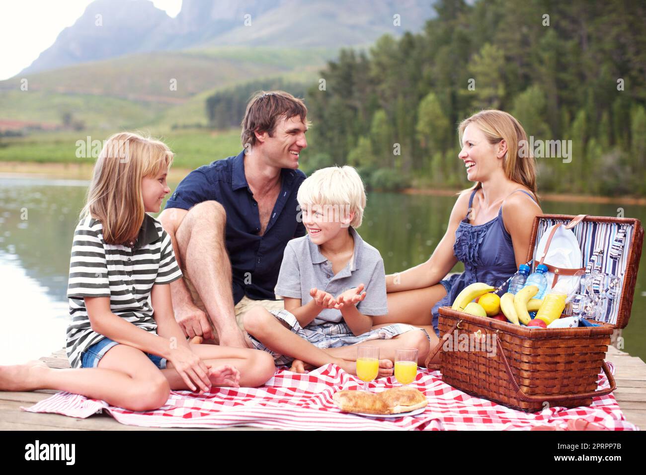 Frische Luft und Zeit für die Familie. Nette junge Familie, die auf einem Steg in der Nähe des Sees Picknick sitzt. Stockfoto