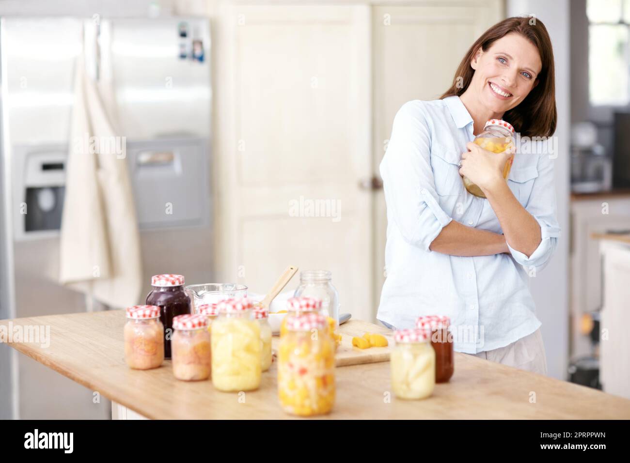 Sie ist stolz auf ihre häuslichen Fähigkeiten. Eine reife Frau, die in der Küche ein Glas an ihre Brust hält. Stockfoto