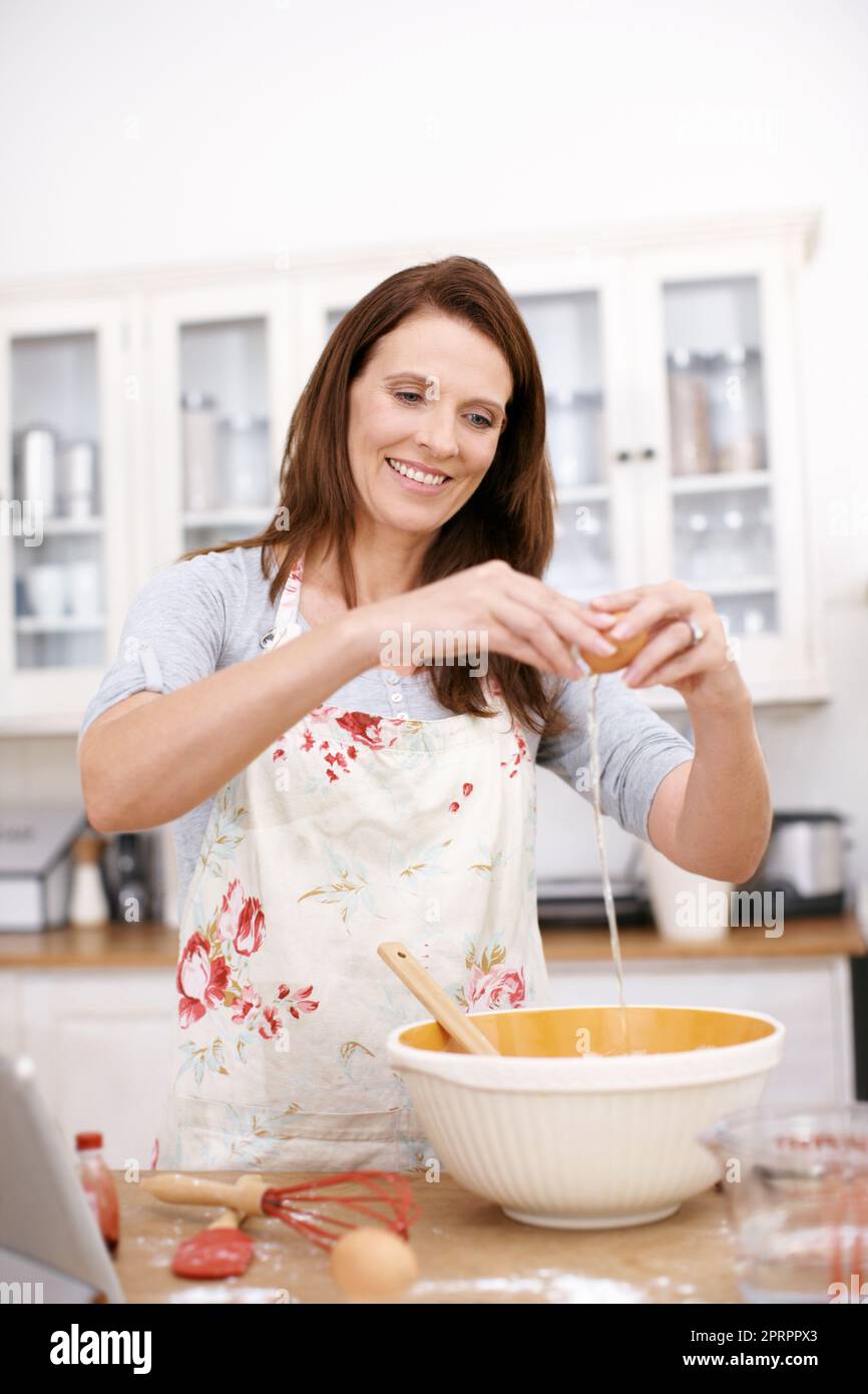 Das Eiweiß vom Eigelb trennen. Eine reife Frau bricht in der Küche ein Ei. Stockfoto