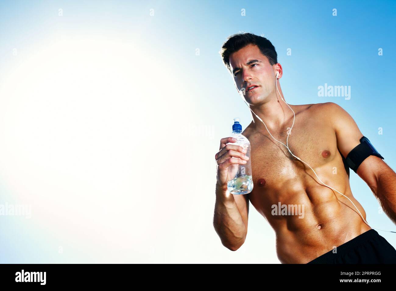 Junger muskulöser Mann mit einer Wasserflasche - Outdoor. Porträt eines jungen muskulösen Mannes mit einer Wasserflasche am wolkigen Himmel - Blick auf den Copyspace. Stockfoto