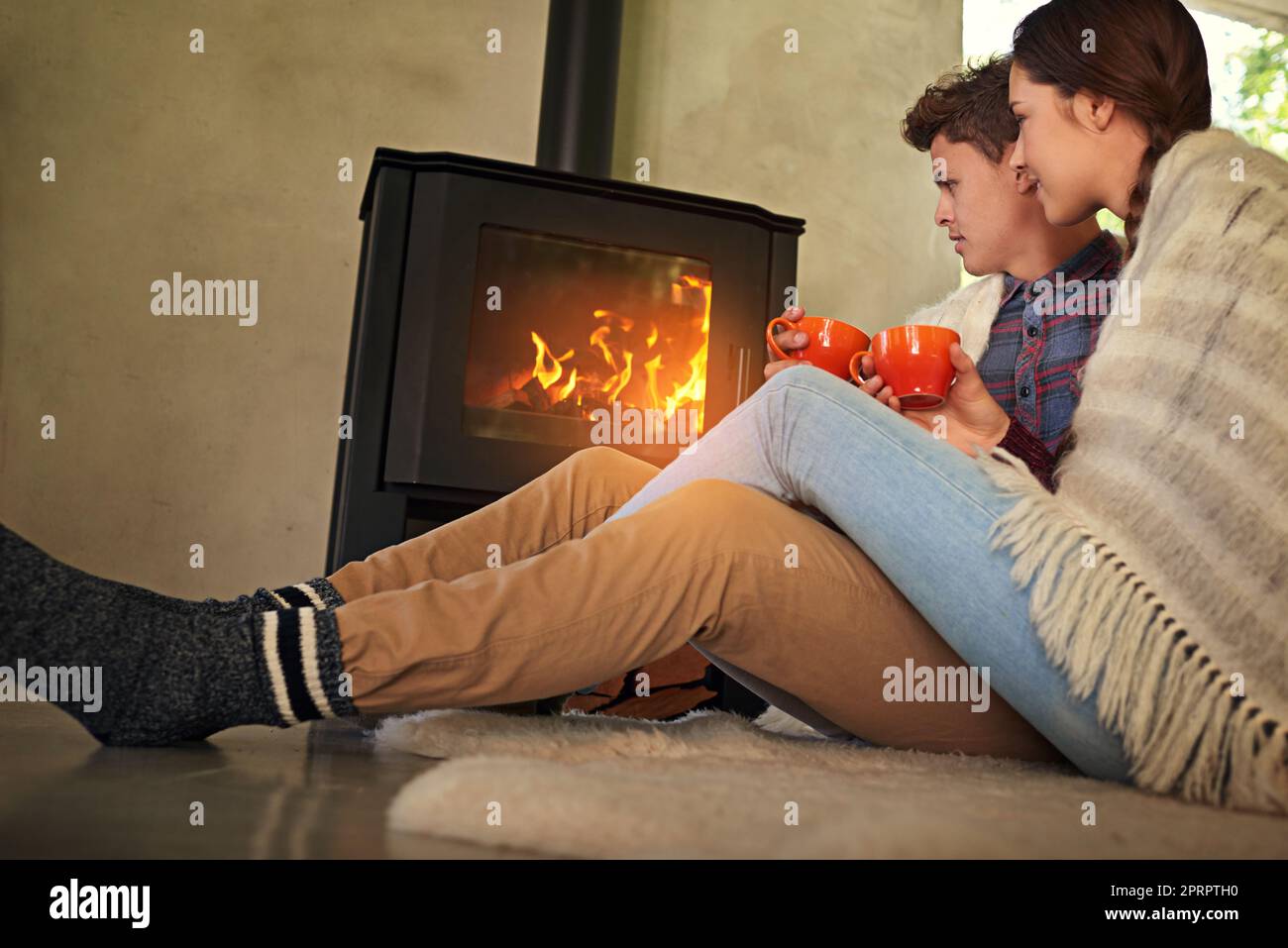 Bleiben Sie gemütlich in dieser Saison. Ein junges Paar trinkt heiße Schokolade am Kamin. Stockfoto