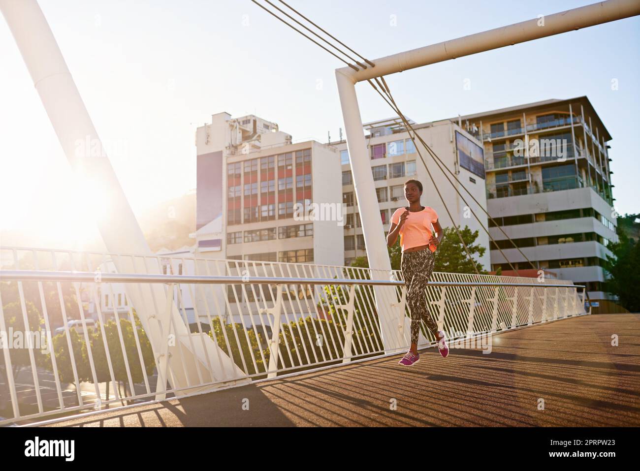 Über die Brücke zu einem gesünderen Lebensstil. Ganzkörperaufnahme einer attraktiven jungen Frau, die im Freien läuft. Stockfoto