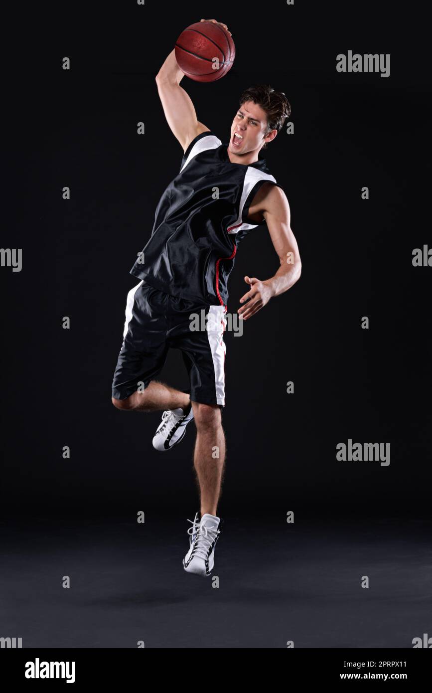 Beim Schießen von Reifen. Ganzkörperaufnahme eines männlichen Basketballspielers in Aktion vor schwarzem Hintergrund. Stockfoto