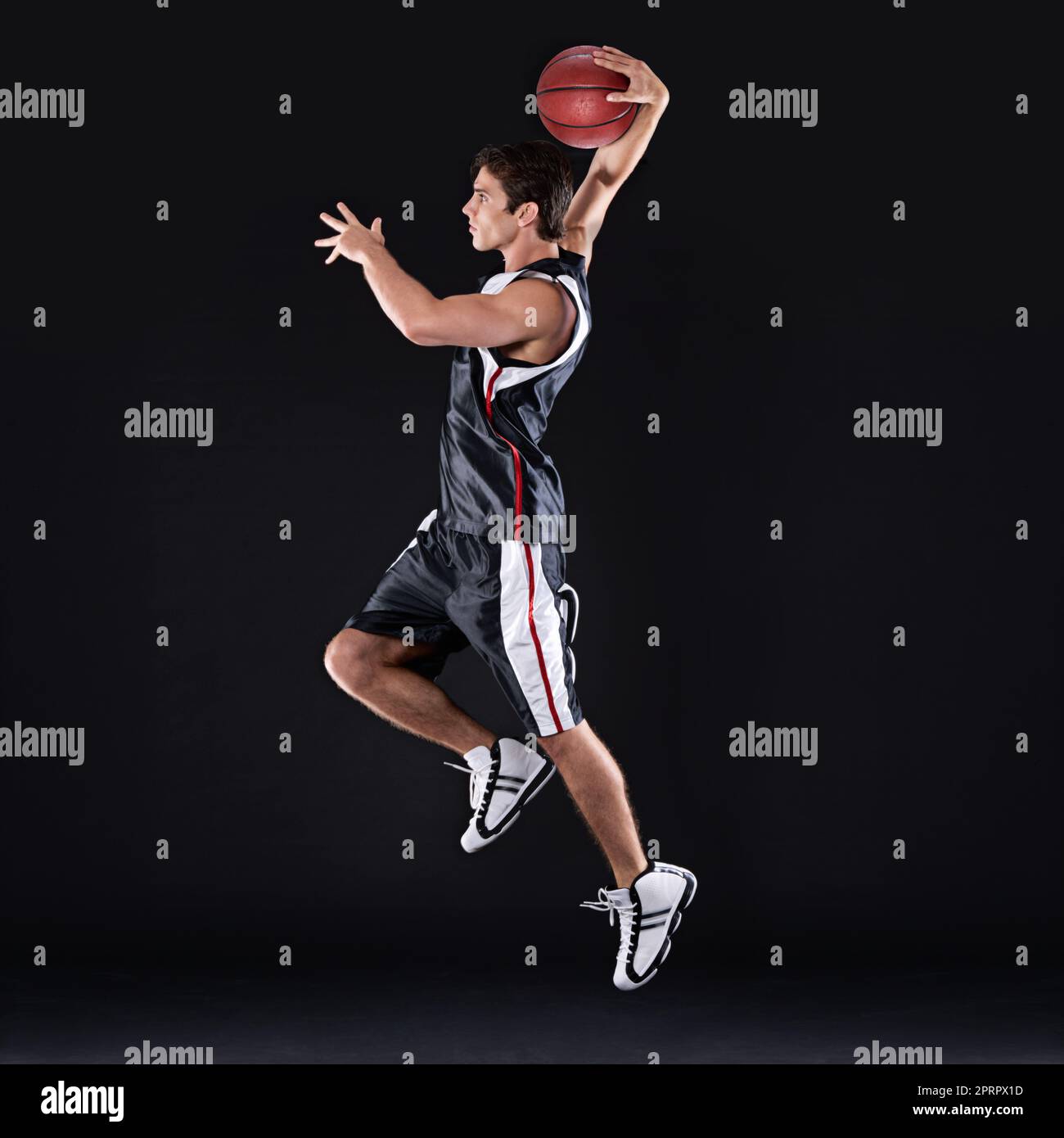 SLAM Dunk. Ganzkörperaufnahme eines jungen männlichen Basketballspielers in Aktion vor schwarzem Hintergrund. Stockfoto