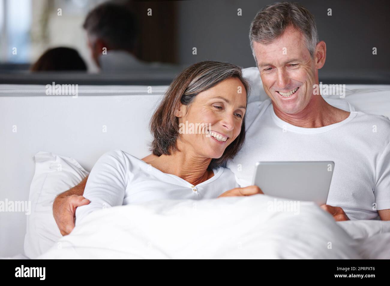 Unterhaltung im Bett. Ein glückliches reifes Paar sitzt im Bett mit einem digitalen Tablet. Stockfoto