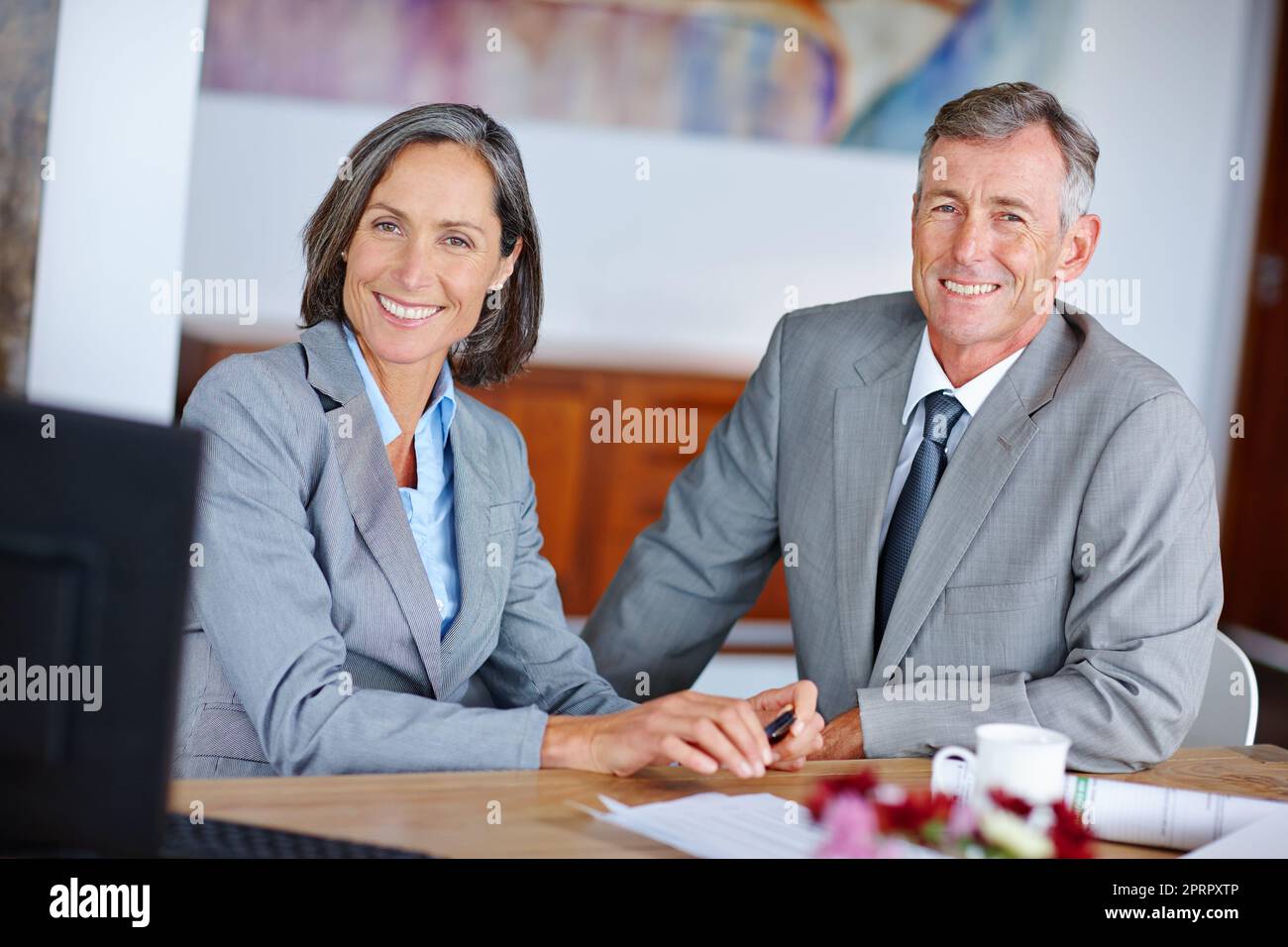 Immer professionell. Porträt von zwei reifen Geschäftskollegen, die nebeneinander an einem Schreibtisch sitzen. Stockfoto