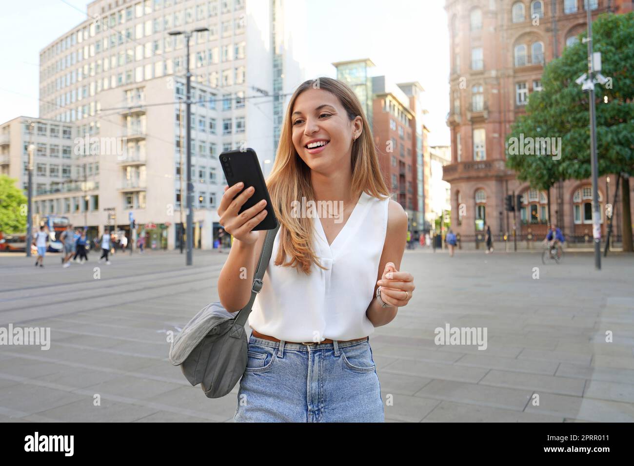 Eine attaktive Geschäftsfrau, die ihr Smartphone beim Spazierengehen in der Stadt Manchester, Großbritannien, beobachtet Stockfoto