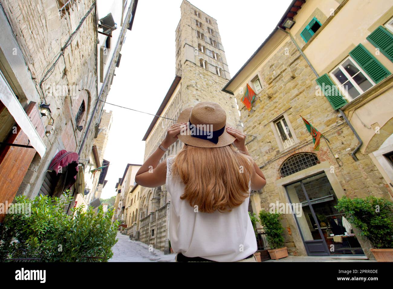 Schöne touristische Mädchen hält Hut zu Fuß im Mittelalter Stadt Arezzo, Toskana, Italien. Niedriger Winkel. Stockfoto