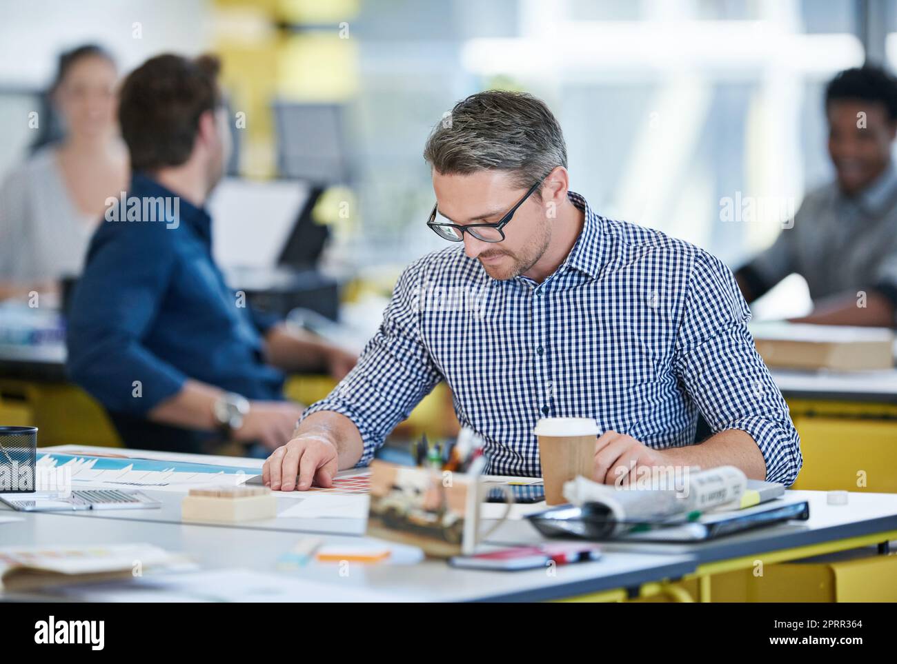 Es gibt kein Problem, das er nicht lösen kann. Ein Büroangestellter sitzt an seinem Schreibtisch mit Kollegen im Hintergrund. Stockfoto