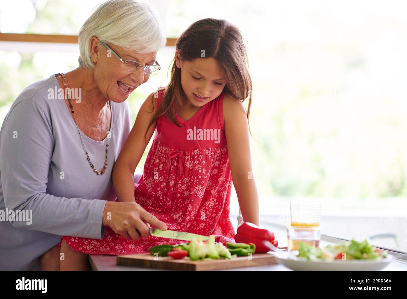Sie liebt es, der Oma zu helfen. Ein kleines Mädchen hilft ihrer Großmutter beim Mittagessen. Stockfoto
