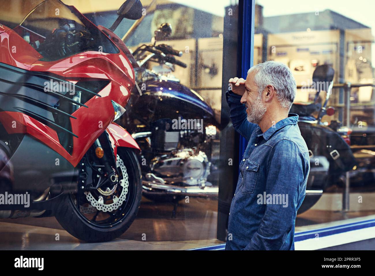 Jeder mann träumt davon. Ein reifer Mann bewundert die Schaufenster eines Motorradladen. Stockfoto