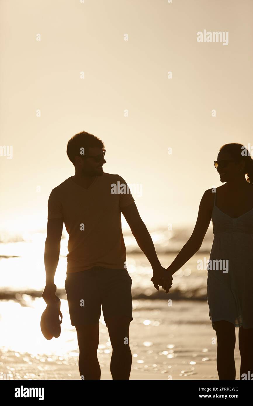 Zeit für einen romantischen Genuss. Ein Paar, das die Hände hielt, silhouted gegen die Sonne über dem Meer. Stockfoto