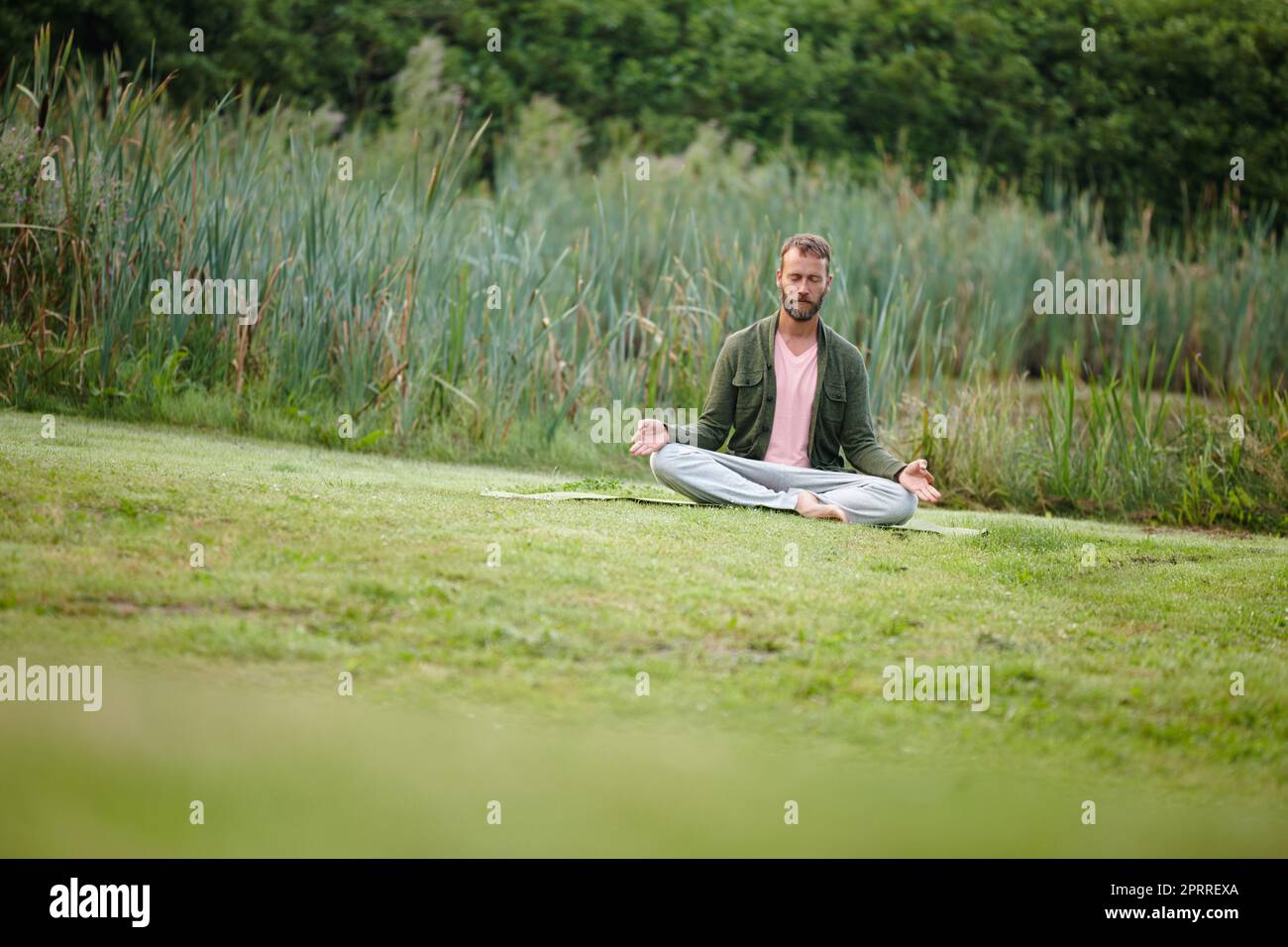 Im Kontakt mit der Natur. Ein hübscher reifer Mann, der in der Lotusposition in der Natur meditiert. Stockfoto