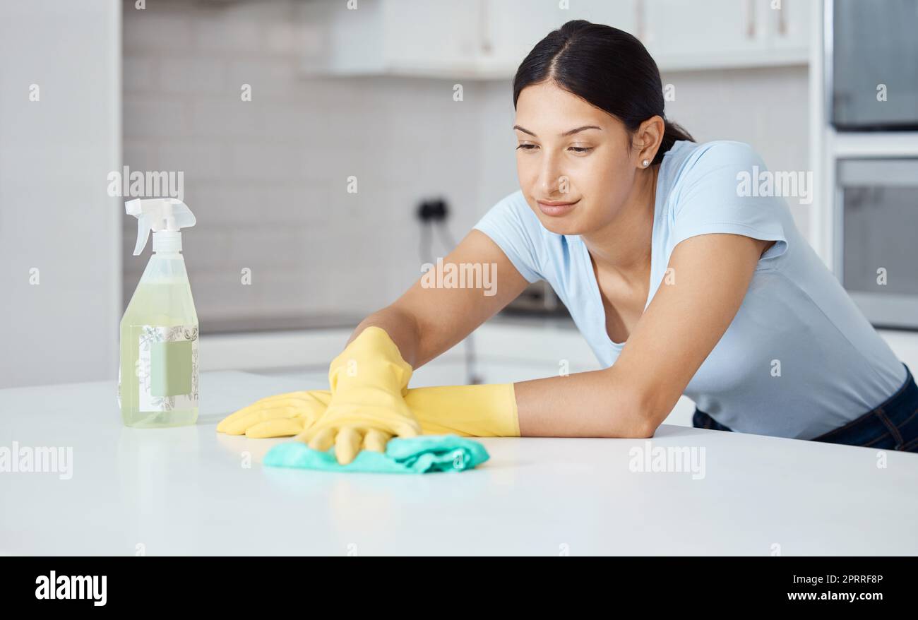 Sauberere Frau reinigt Küchentheke mit Tuch, Sprühflasche und Gummihandschuhen in moderner Inneneinrichtung. Servicemitarbeiter, der mit Seifenlauge, Hygieneartikeln oder Wischflächen für die Frühjahrsputz arbeitet Stockfoto