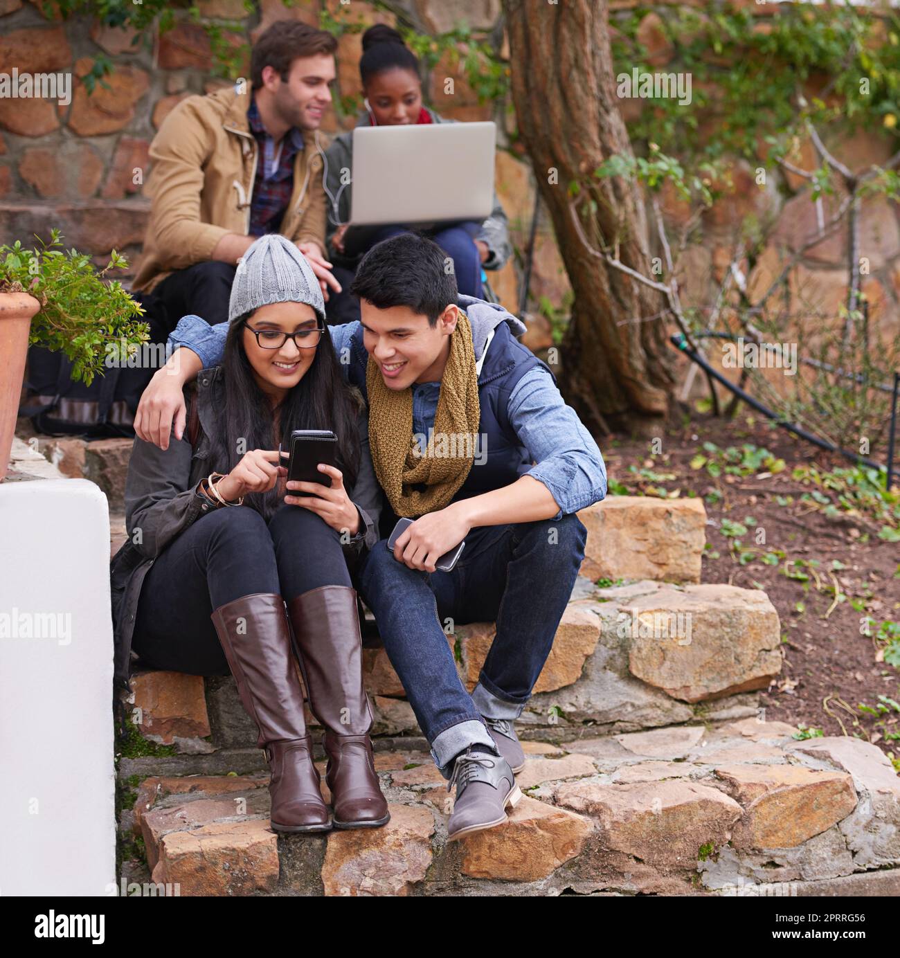 Es geht um mehr als nur um Bildung. Ein Paar, das sich etwas auf einem Handy ansieht, während andere Studenten im Hintergrund sitzen. Stockfoto