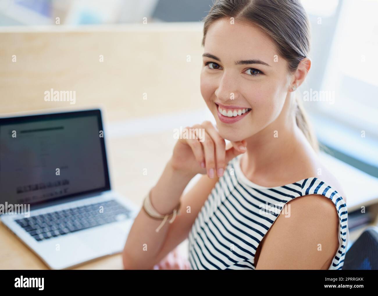 Ihre Karriere ist im Trend. Porträt einer lächelnden jungen Geschäftsfrau, die mit einem Laptop an einem Tisch in einem Büro sitzt. Stockfoto