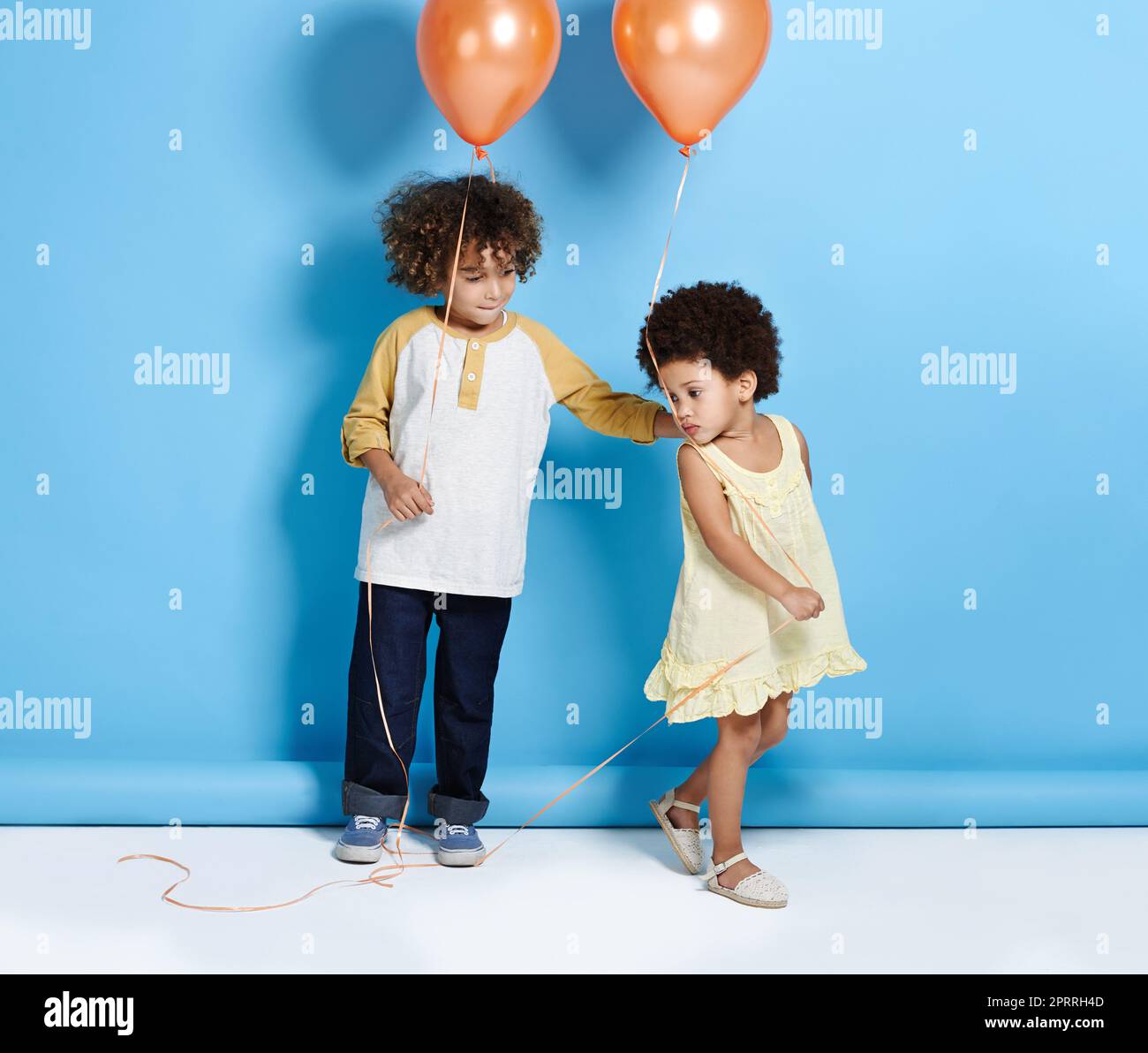 Ein kleines Mädchen und ein Junge halten einen Ballon über einem blauen Hintergrund. Stockfoto