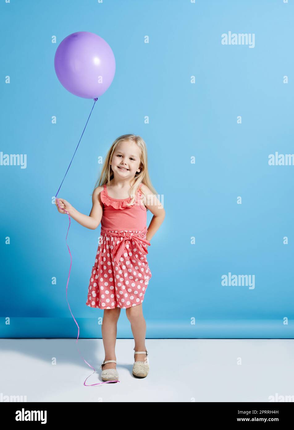 Niemand kann mit einem Ballon entjubelt werden. Ein niedliches kleines Mädchen hält einen Ballon über einem blauen Hintergrund. Stockfoto