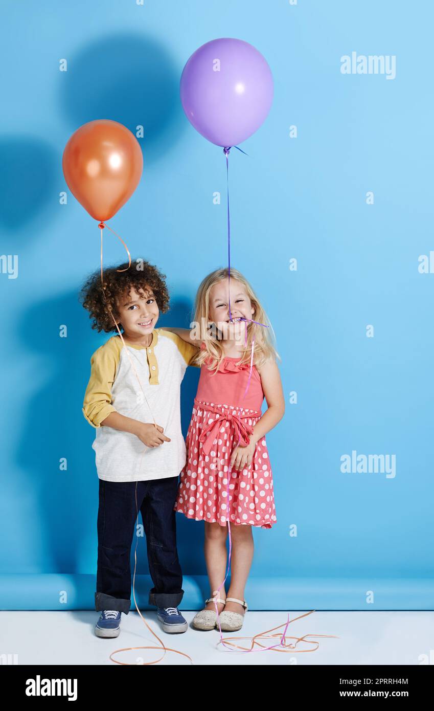 Lasst uns mitreißen. Porträt eines niedlichen kleinen Mädchens und Jungen, der einen Ballon auf einem blauen Hintergrund hält. Stockfoto