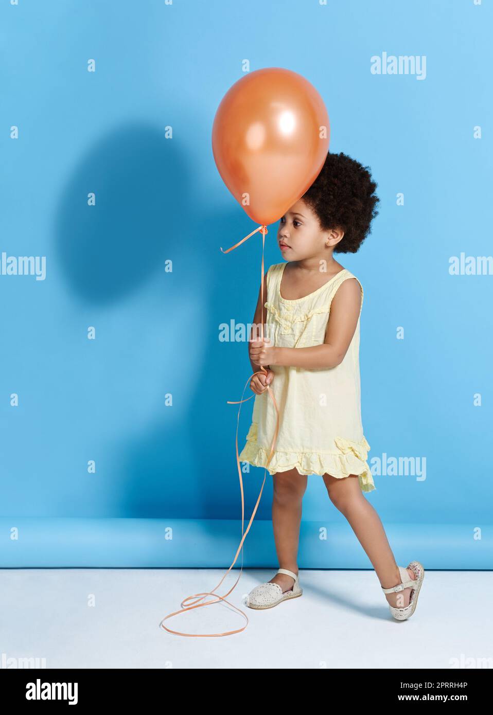 Sollen wir Mr. Balloon tanzen? Ein niedliches kleines Mädchen, das einen Ballon über einem blauen Hintergrund hält. Stockfoto
