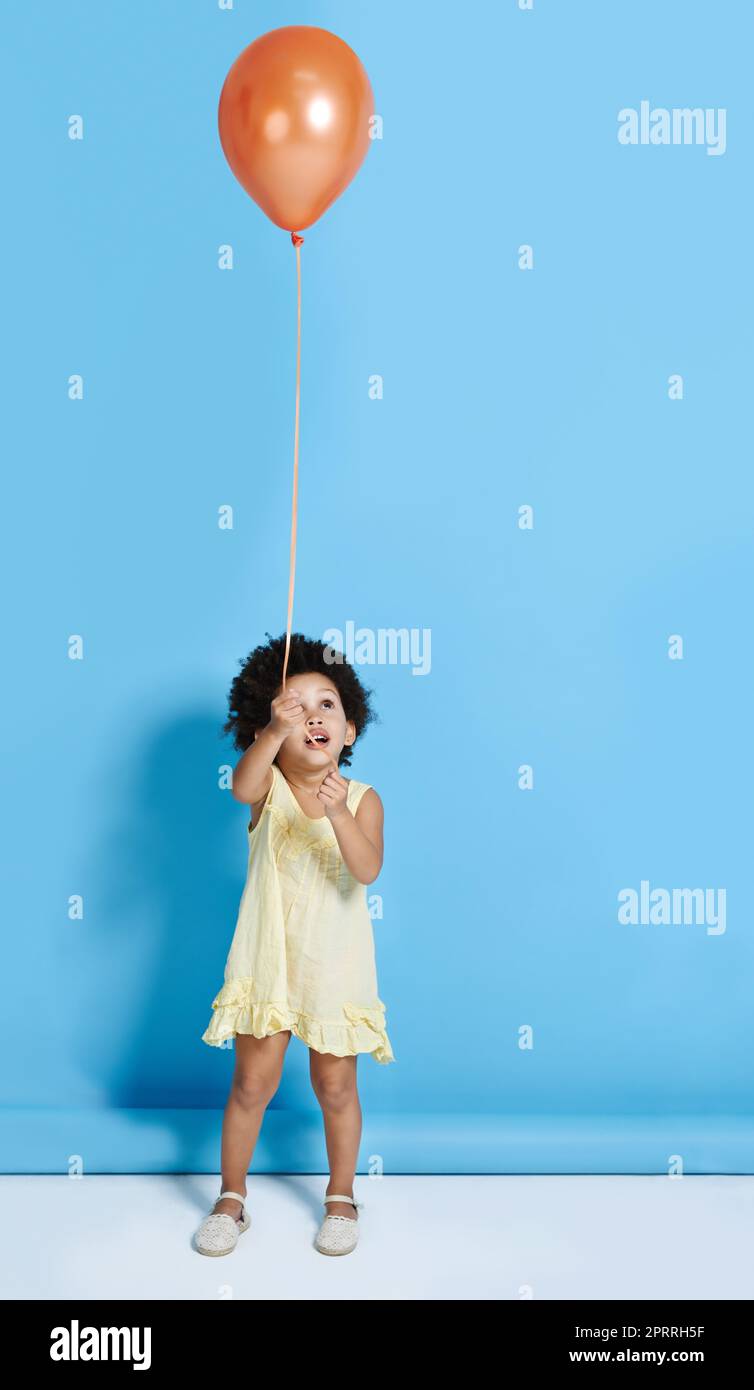 Hey Warte auf mich., ein niedliches kleines Mädchen, das einen Ballon auf einem blauen Hintergrund hält. Stockfoto