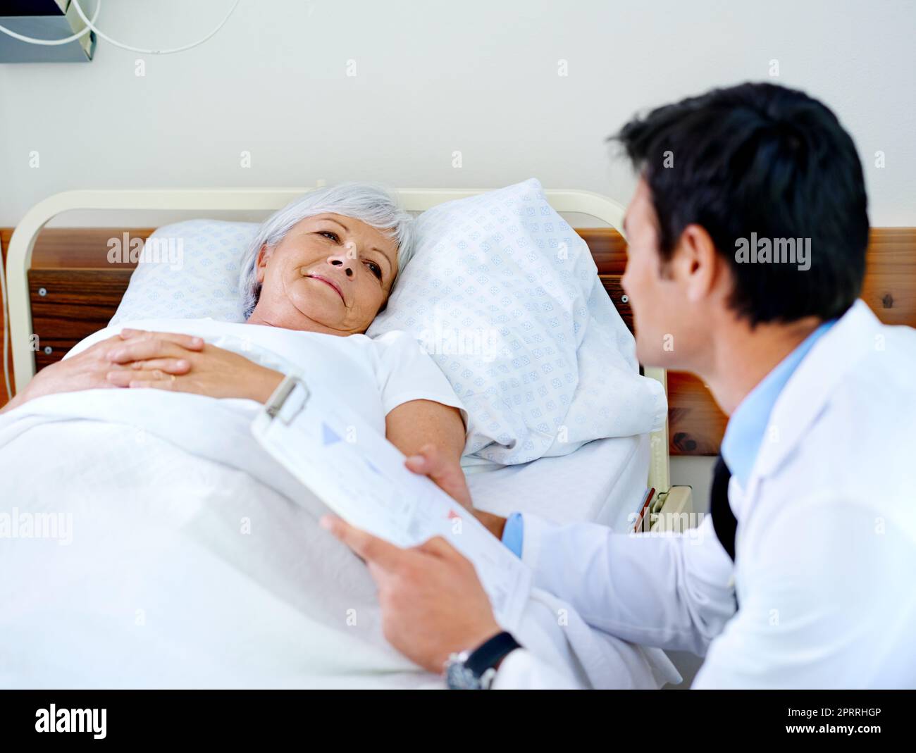 Ein Arzt bespricht die Testergebnisse mit seinem älteren Patienten, der sich in einem Krankenhausbett befindet. Stockfoto