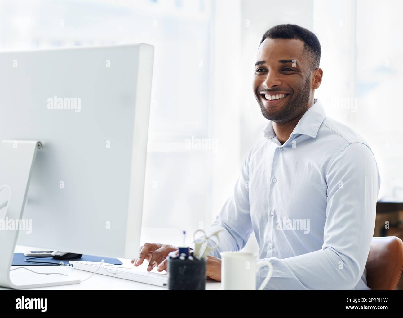 Zur Arbeit zu kommen ist keine lästige Pflicht für ihn. Ein hübscher junger afroamerikanischer Geschäftsmann, der an seinem Schreibtisch arbeitet. Stockfoto