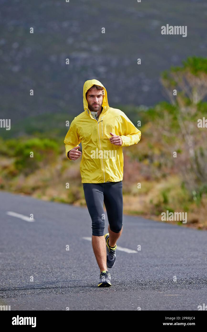 Hingabe an das ultimative Ziel. Ein hübscher junger Mann, der auf einer Straße mit Busch im Hintergrund läuft. Stockfoto