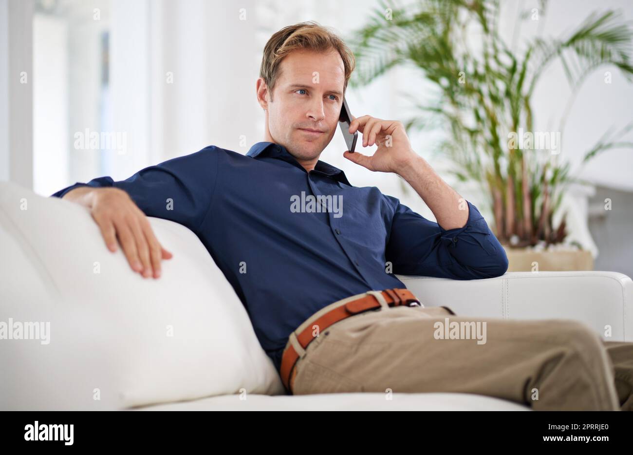 Couch-Gespräche. Ein hübscher Mann, der zu Hause auf seinem Handy spricht. Stockfoto