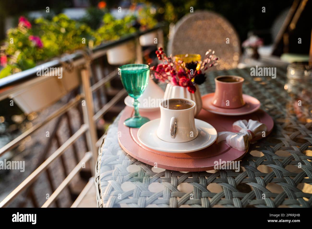 Türkische Kaffeetassen, serviert im Freien mit Wasserblumen und köstlichem Dessert in romantischer Anordnung auf einem Glastisch Stockfoto