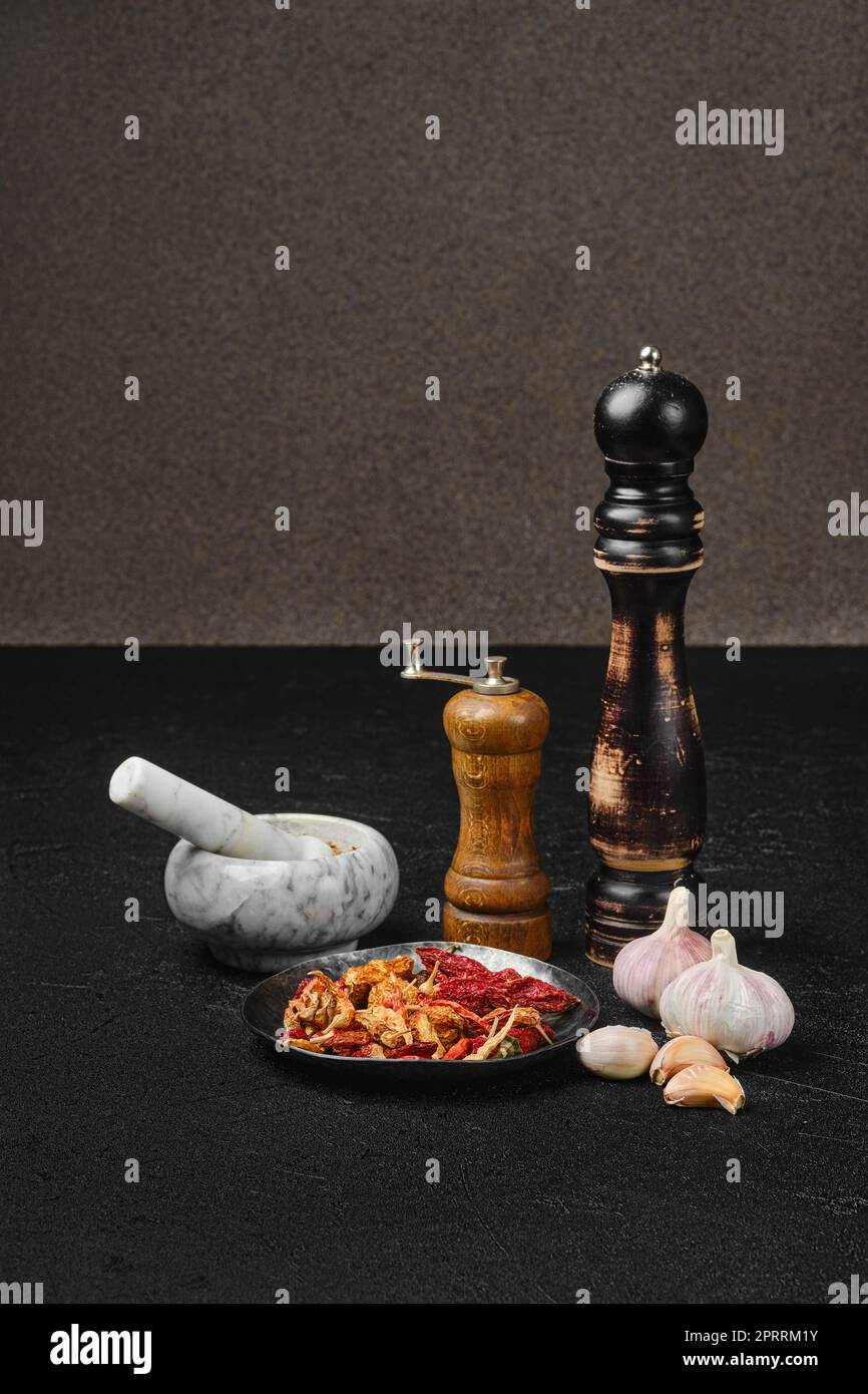 Gewürzmörtel, Mühle und Mahlwerk auf einem Tisch mit Knoblauch und trockenem Chilipfeffer Stockfoto