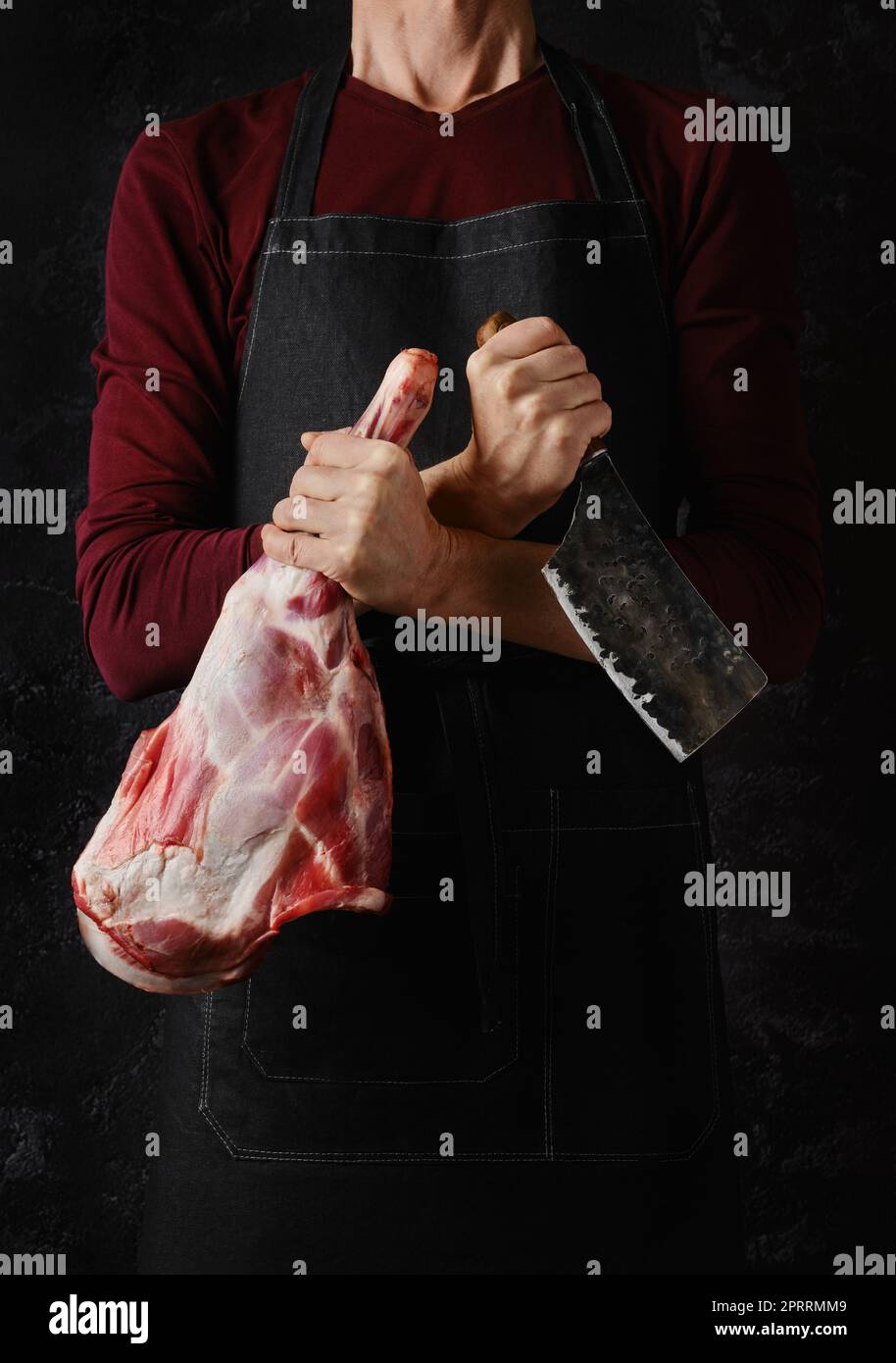 Der Metzger hält rohe Lammkeule in einer Hand und Hackbeil in einer anderen Stockfoto