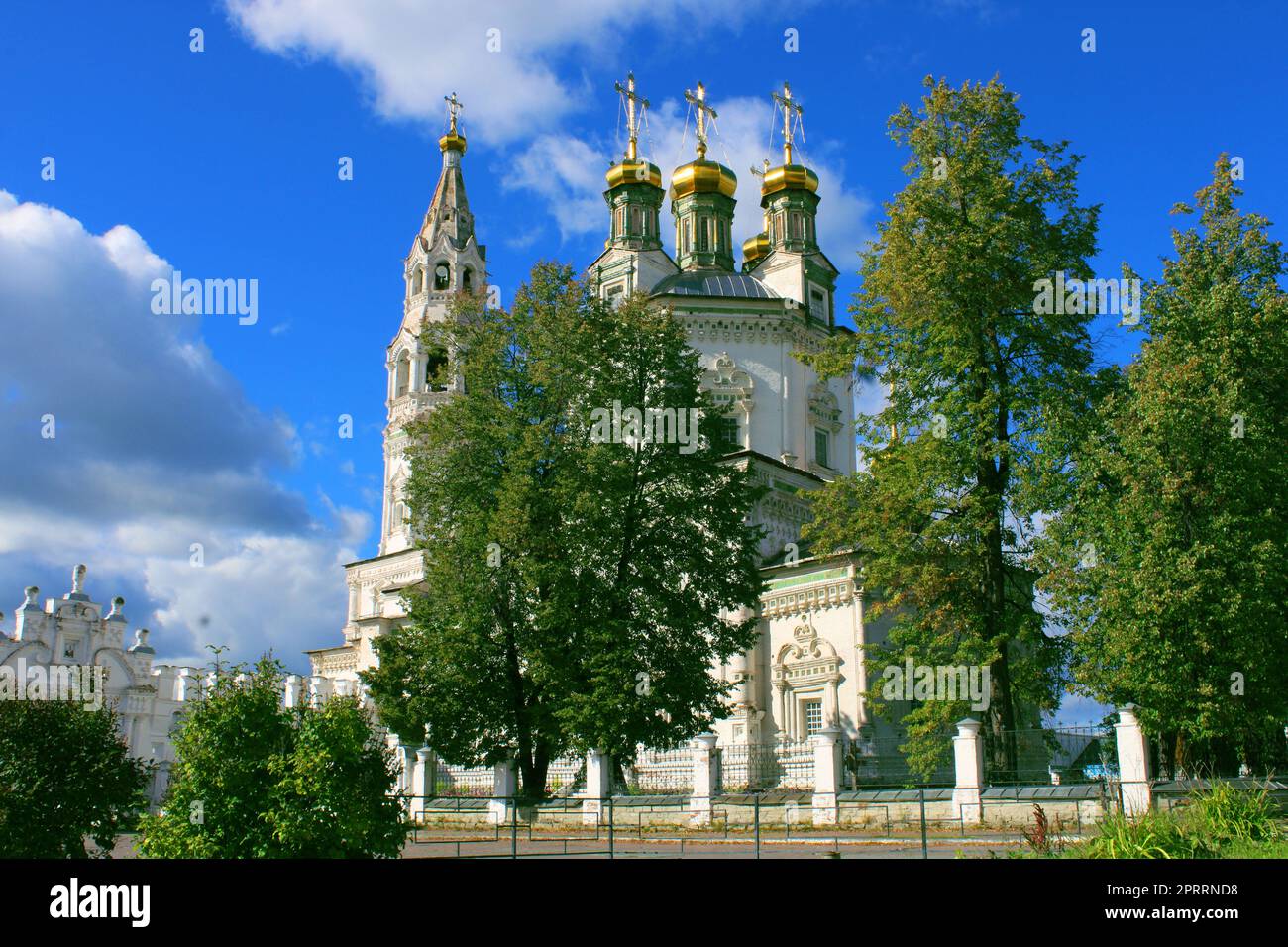 Eine große alte Kirche aus weißem Stein vor dem Hintergrund großer Bäume und eines blauen Himmels Stockfoto