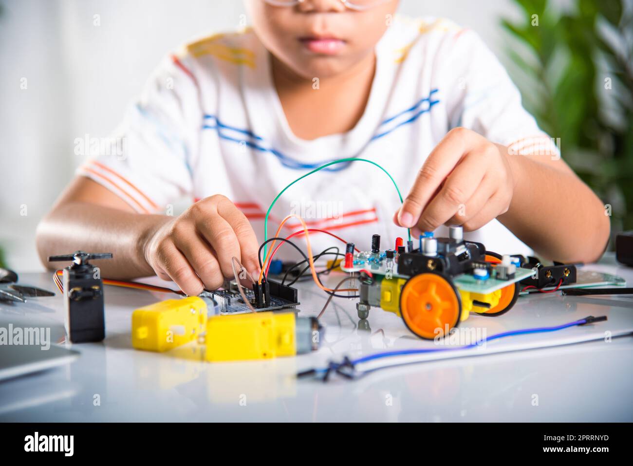 Asiatischer Junge stecken Energie-und Signalkabel an Sensor-Chip mit Arduino Roboterauto Stockfoto
