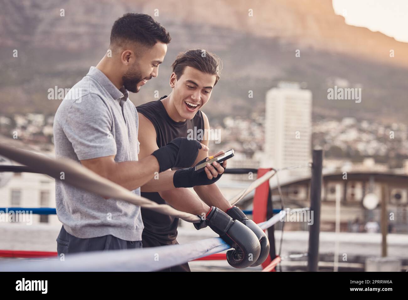 Boxer und Trainer mit Telefon nach Training, Training oder Workout, um online ein Meme für soziale Medien zu lesen. Ein Sportler lächelt und lacht, nachdem er mma, muay thai und Boxen im Freien in einem Kampfring trainiert hat Stockfoto