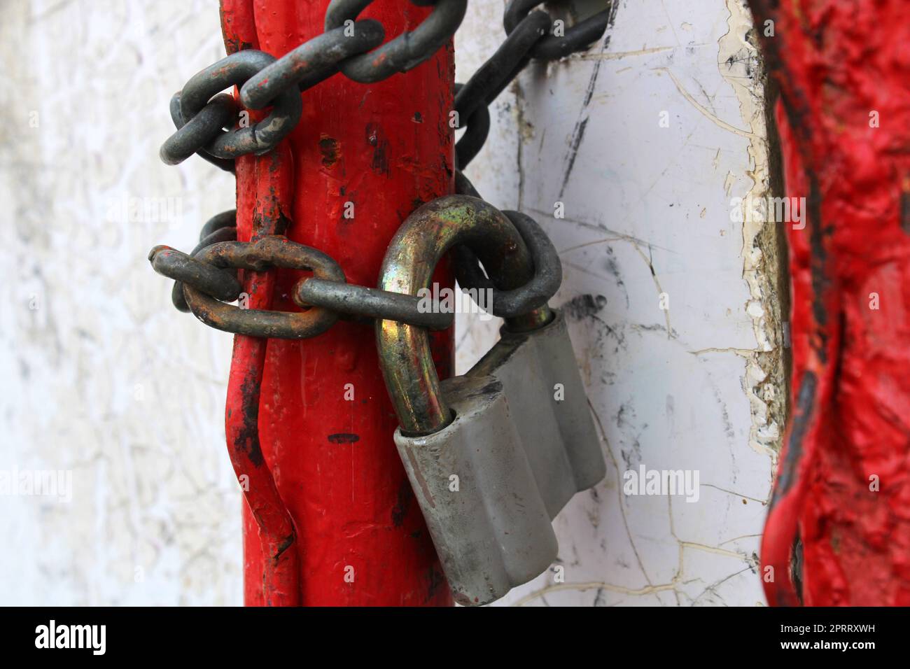 Ein altes Vorhängeschloss an einer rostigen Kette, das um rote Rohre gewickelt war. Stockfoto