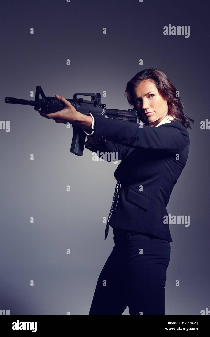 Bereit, dich zu erschießen. Eine junge Geschäftsfrau in Anzug und Krawatte mit Gewehr. Stockfoto