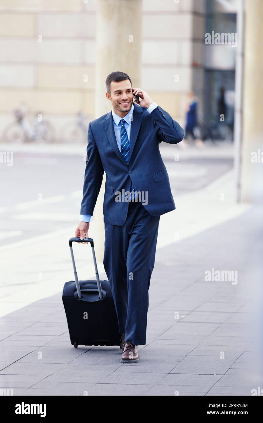Auf dem Weg zur Abflughalle... Ein hübscher junger Geschäftsmann auf seinem Handy, während er mit seinem Gepäck zum Flughafen ging. Stockfoto