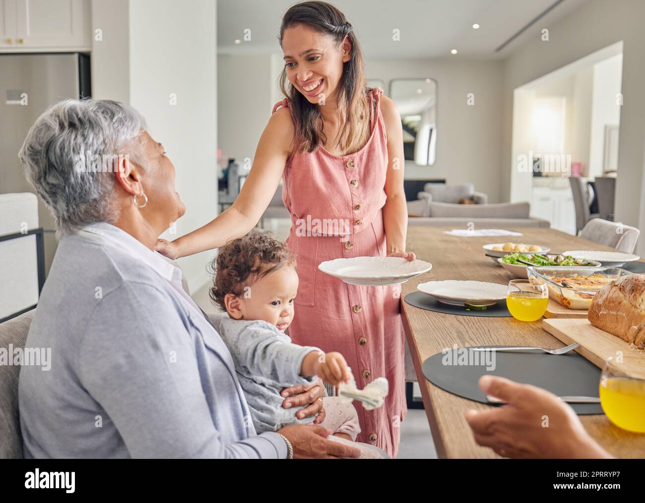 Mama, Baby und Großmutter essen am Tisch, verbinden und teilen Essen und Liebe zu Hause. Glückliche, lächelnde und entspannte Frauen, die sich beim Essen anfreunden, die Zeit mit der Familie genießen und liebevoll und fürsorglich sind Stockfoto