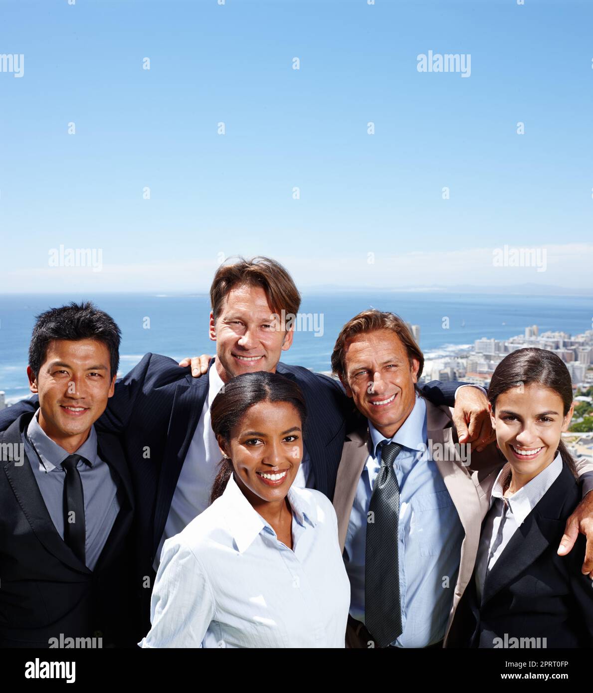 Neue Verbindungen an der frischen Luft bilden. Gruppenaufnahme von lächelnden Geschäftsleuten mit einer Küstenstadt im Hintergrund. Stockfoto