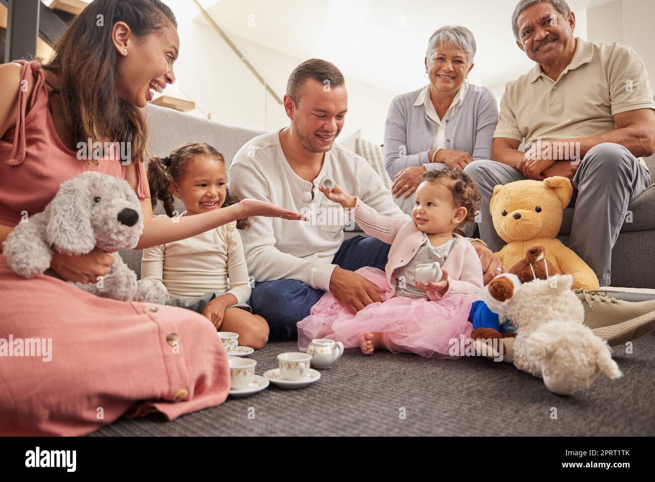 Großes Familienporträt im Kinderzimmer mit Teeparty Spielzeugen zum Spielen und Zusammenhalten auf dem Boden. Glückliche Großeltern, Mutter und Vater mit dem Baby in ihrem Familienhaus, das Spaß hat, auf dem Boden zu sitzen Stockfoto