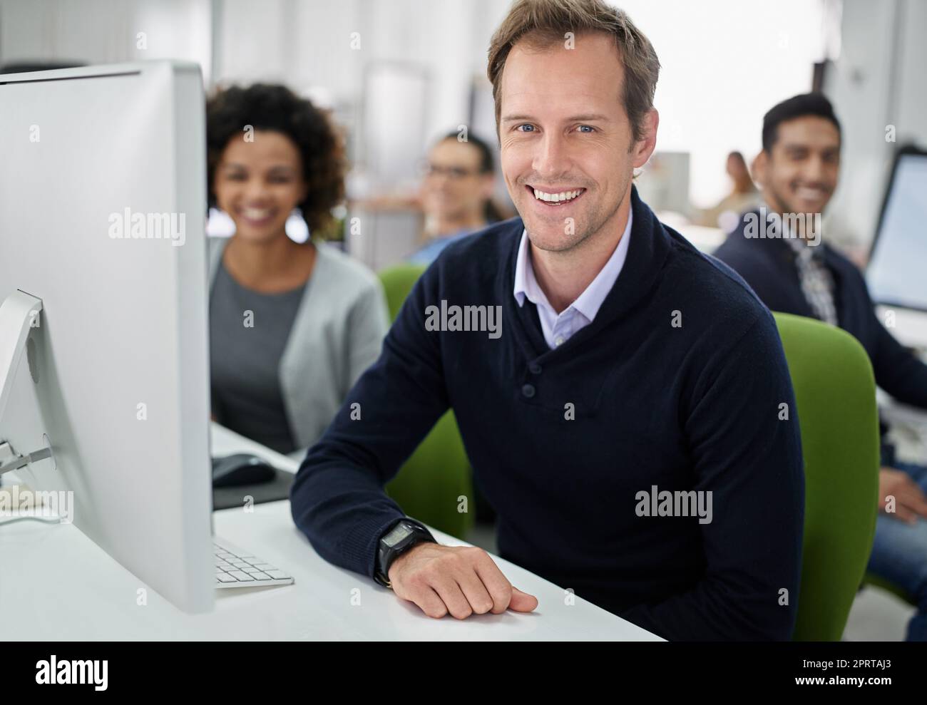 Unser Arbeitsplatz hat eine positive Einstellung. Porträt eines lächelnden Geschäftsmannes mit seinen Mitarbeitern im Hintergrund. Stockfoto