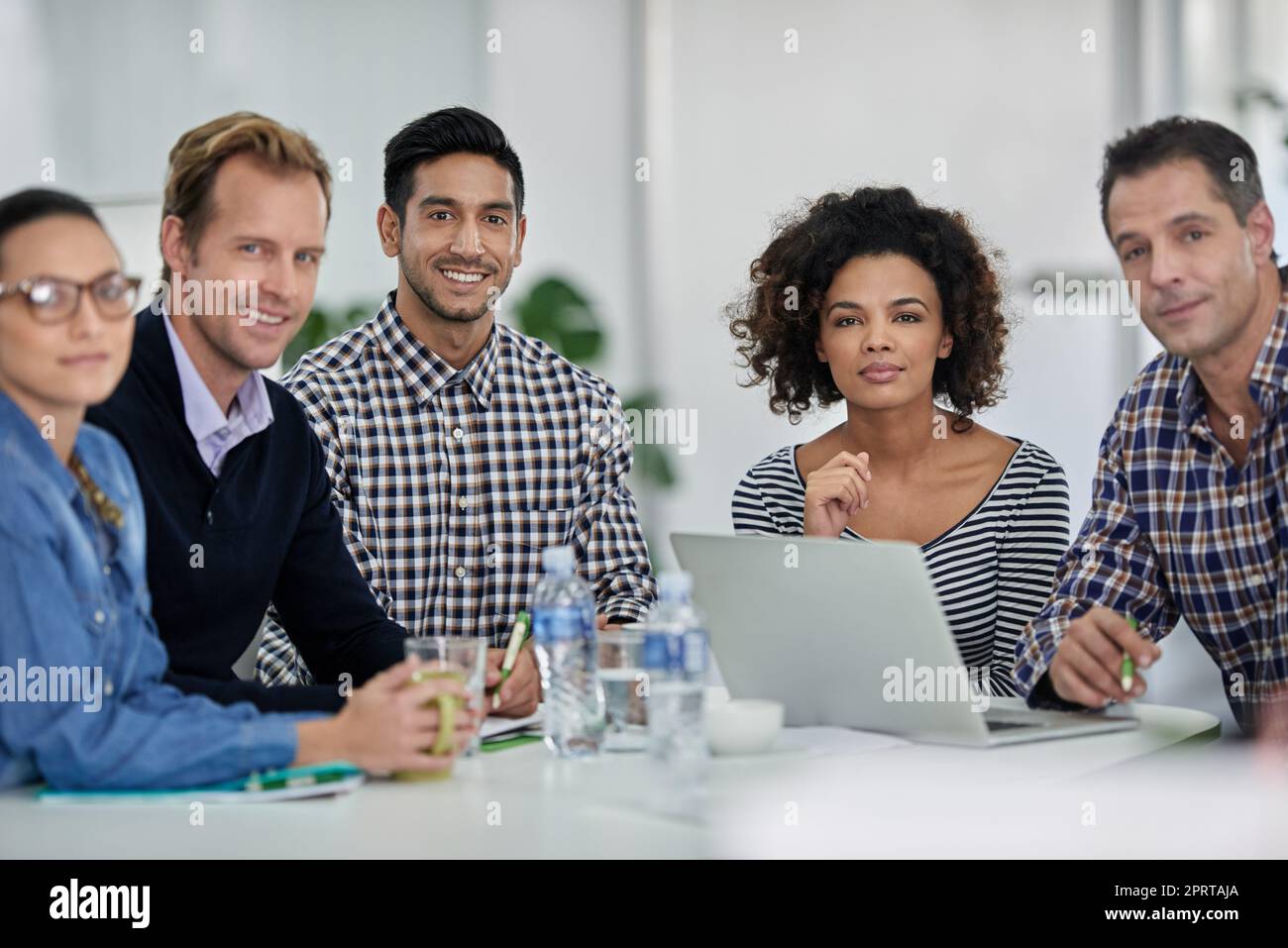 Starkes und selbstbewusstes Team. Gruppe von Kollegen, die an einem Besprechungstisch sitzen und die Kamera lächeln. Stockfoto