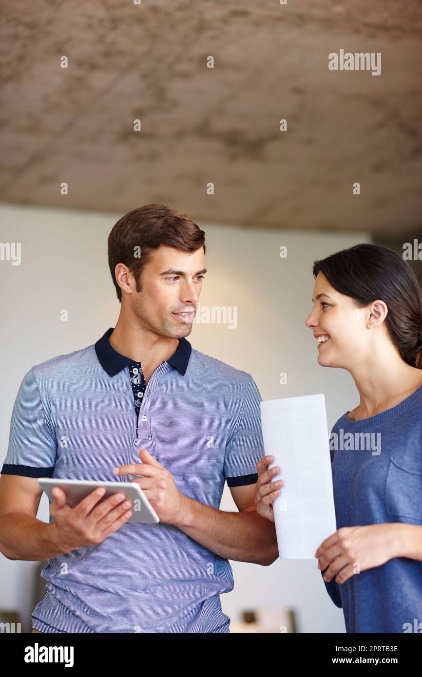 Das Technologie-Team. Ein Mann mit einem digitalen Tablet, während seine Frau mit einem Dokument zur Verfügung steht. Stockfoto