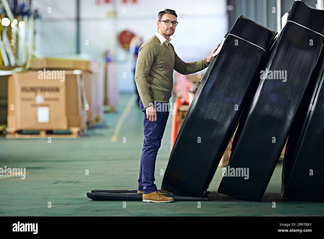 Unser Produkt ist unschlagbar: Ein Mann, der neben großen Kunststoffrollen in einem großen Lager steht. Stockfoto