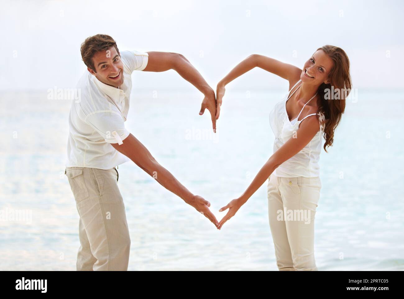 Herzförmiges Glück - Konzept. Ein junges Paar, das am Strand ein herzförmiges Schild mit den Armen macht. Stockfoto