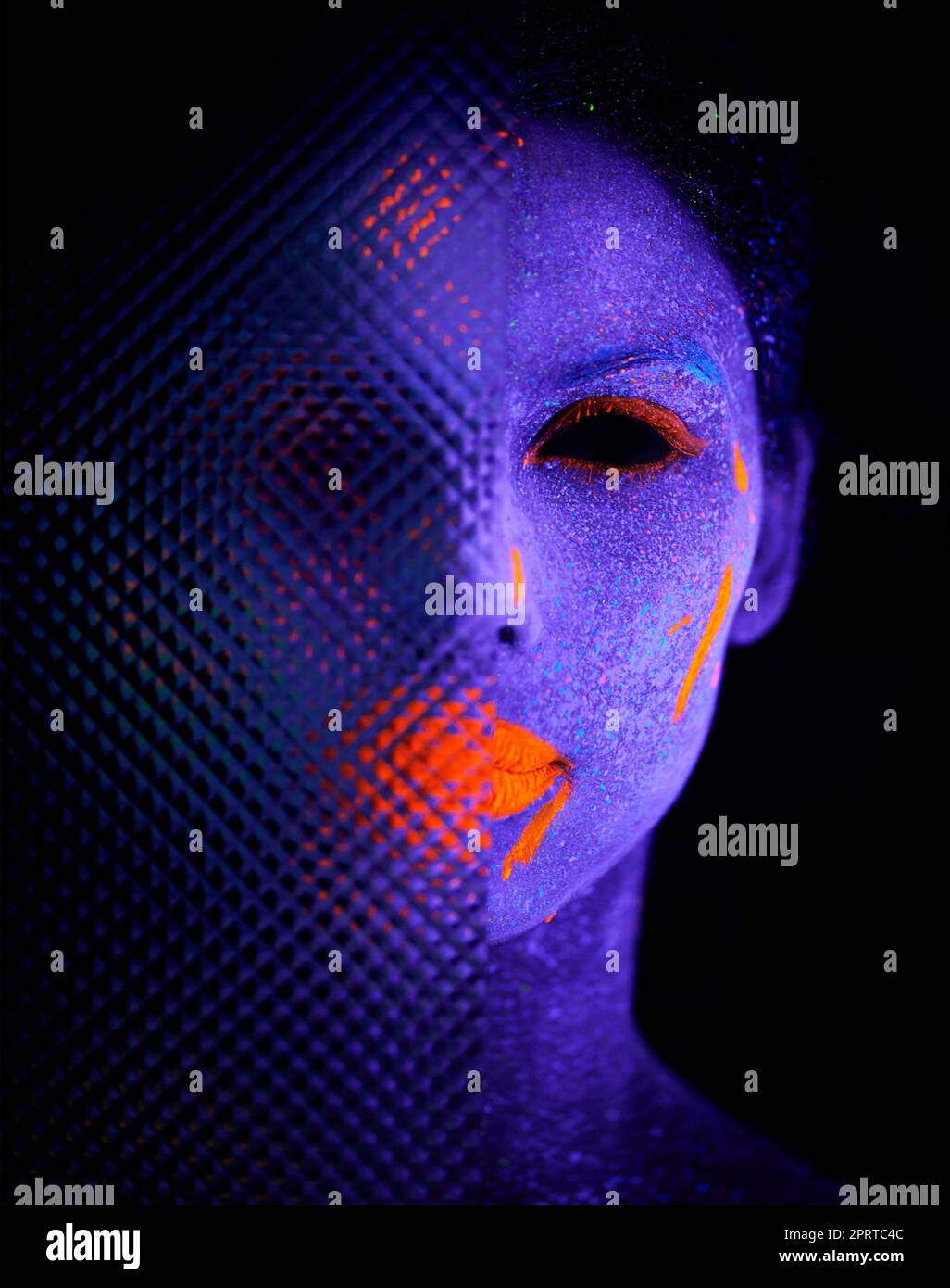 Dunkle Enthüllungen. Eine junge Frau posiert mit Neonfarbe auf ihrem Gesicht. Stockfoto