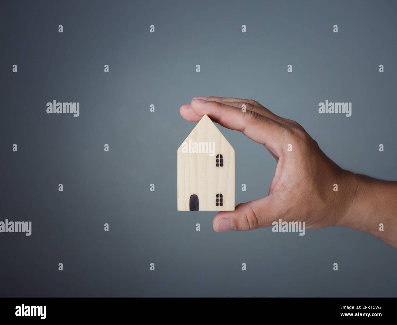 Konzept des Verkaufs eines Hauses. Eine Hand hält ein Modellhaus auf grauem Hintergrund. Immobilienmakler bieten Haus, Sachversicherung und Sicherheit, erschwingliche Wohnkonzepte, Hausversicherungsvermittler, Verkäufer. Stockfoto