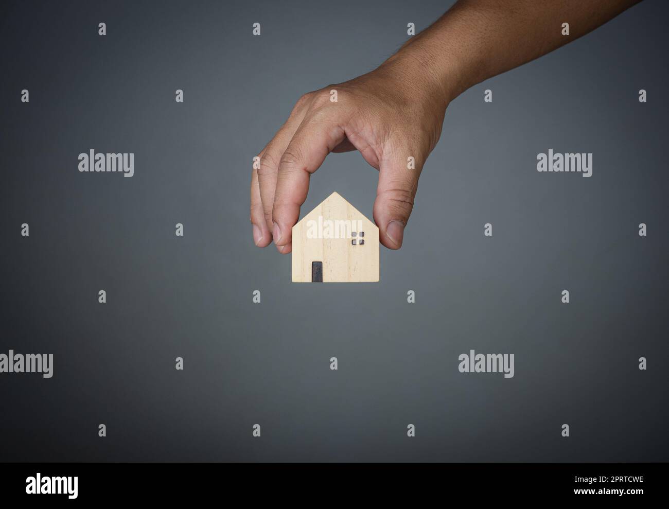 Konzept des Verkaufs eines Hauses. Eine Hand hält ein Modellhaus auf grauem Hintergrund. Immobilienmakler bieten Haus, Sachversicherung und Sicherheit, erschwingliche Wohnkonzepte, Hausversicherungsvermittler, Verkäufer. Stockfoto